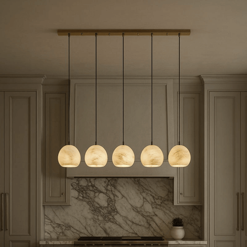 The Auris 5-Light Marble Chandelier by Morsale.com, featuring marble-patterned glass shades and adjustable cords, hangs above a kitchen island with beige cabinets and a marble backsplash in the background.