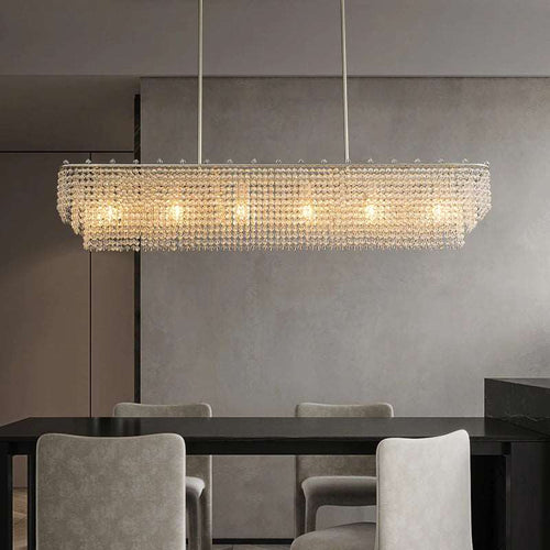 A modern dining room features the Alleri Crystal Dining Room Chandelier by Morsale.com hanging above a dark table with four light gray upholstered chairs, set against neutral gray walls for a look of modern functionality and crystal elegance.