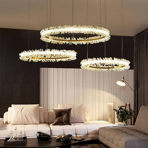 Modern living room with a beige sectional sofa, decorative pillows, floor lamp, and three Capri 3-Ring Crystal Chandeliers by Morsale.com featuring handmade clear crystals emitting warm light above the coffee table for a sophisticated touch.
