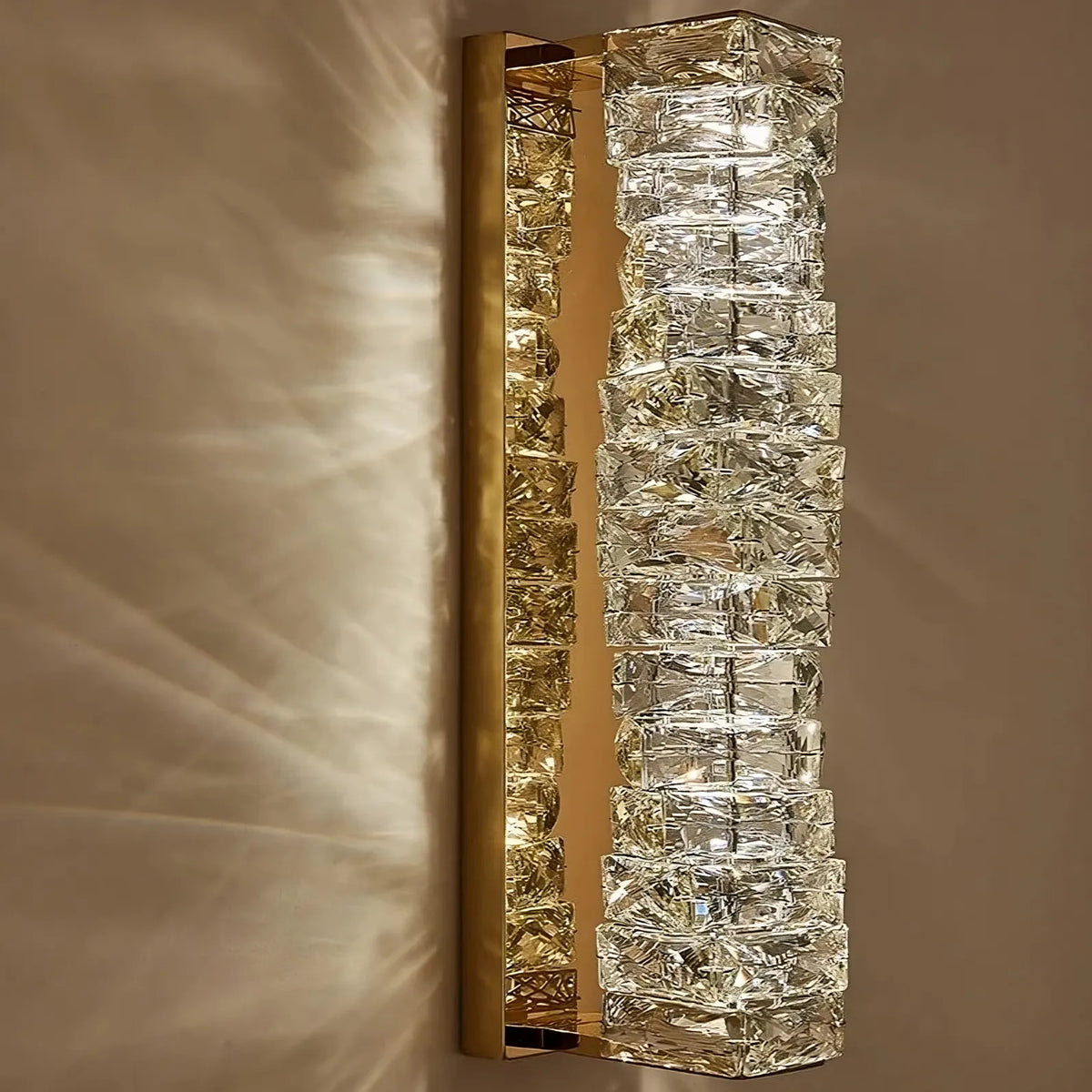 A modern Morsale.com Bacci wall sconce featuring a vertical row of square handmade crystals that emit a warm, soft glow, casting geometric shadows on the wall.