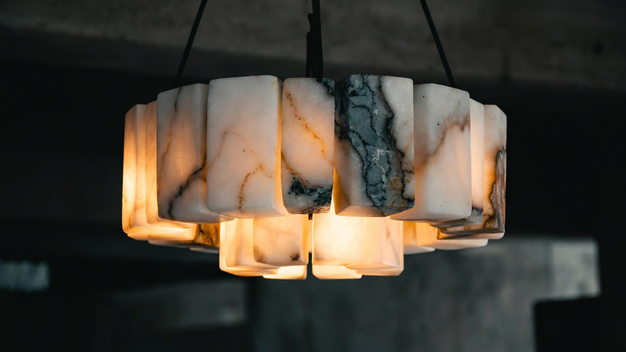 Hand-carved marble chandelier glowing softly, showing the natural veining and warm candlelight-like diffusion of authentic natural stone lighting from Morsale.