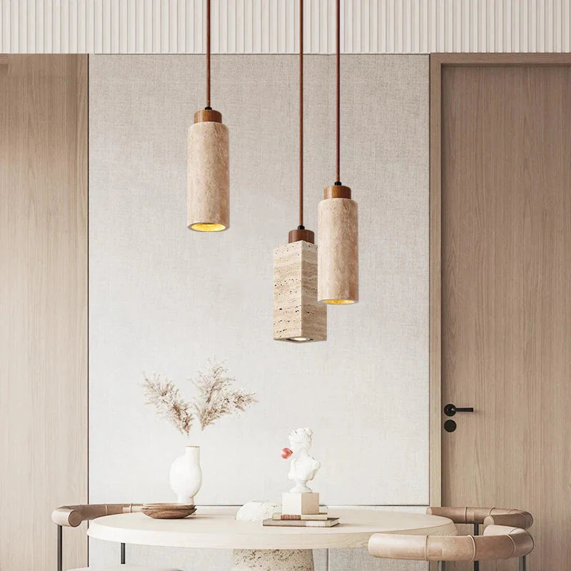 Three Natural Travertine Pendant Lights from Morsale.com with cylindrical beige shades hang from the ceiling. The central light, elegantly crafted from travertine, showcases a square, stone-like shade, while the two on either side feature round, smooth sh