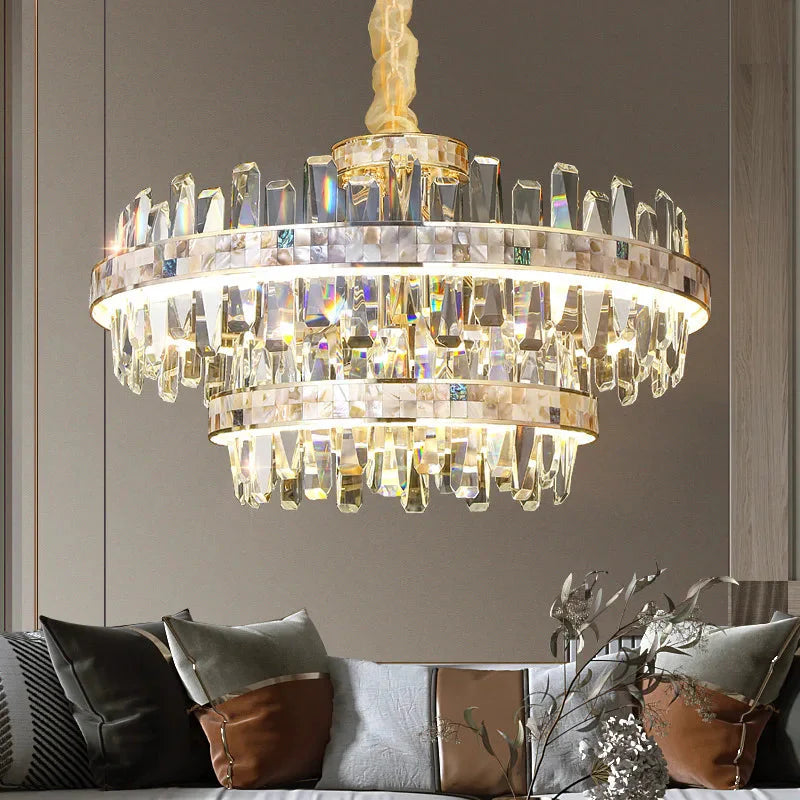 The Calvi Crystal Chandelier by Morsale, a luxurious masterpiece of modern style lighting, is suspended above a sleek living room featuring a gray sofa adorned with decorative pillows. The chandelier's LED lights produce a sparkling effect, beautifully il