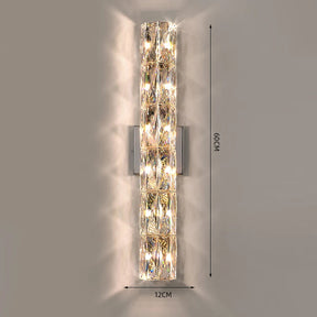 The Bacci Crystal Wall Light Sconce by Morsale.com is a vertical, cylindrical indoor lighting fixture with a polished chrome finish and handmade crystal embellishments. Measuring 60 cm in height and 12 cm in width, it emits a warm, diffused light that creates intricate patterns on the wall.