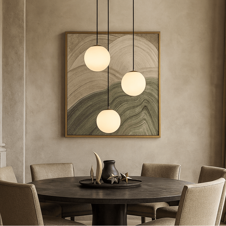 A round dining table with beige chairs is set with decor. Above, the Morsale Brighton Marble Chandelier hangs, while an abstract artwork with soft curved shapes adds interest to the wall behind.