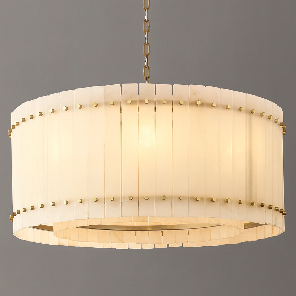
                  
                    The Valmont Marble Round Chandelier 24" by Morsale features vertical white panels and gold accents, suspended on a gold chain, casting warm, diffused light against a plain gray background.
                  
                