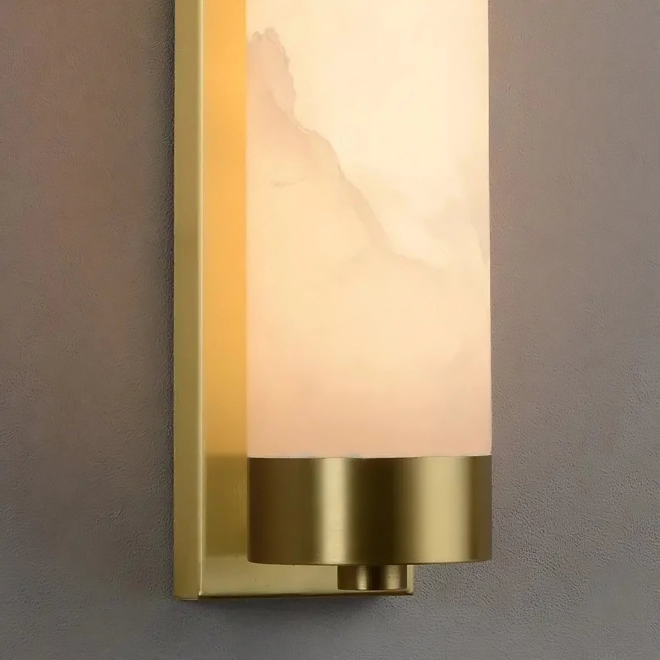 A close-up of a 23" Natural Marble & Brass Wall Light by Morsale with a rectangular brass base and a cylindrical white alabaster shade against a gray wall. This sustainable luxury piece features an energy-efficient LED, emitting a warm, subtle glow.