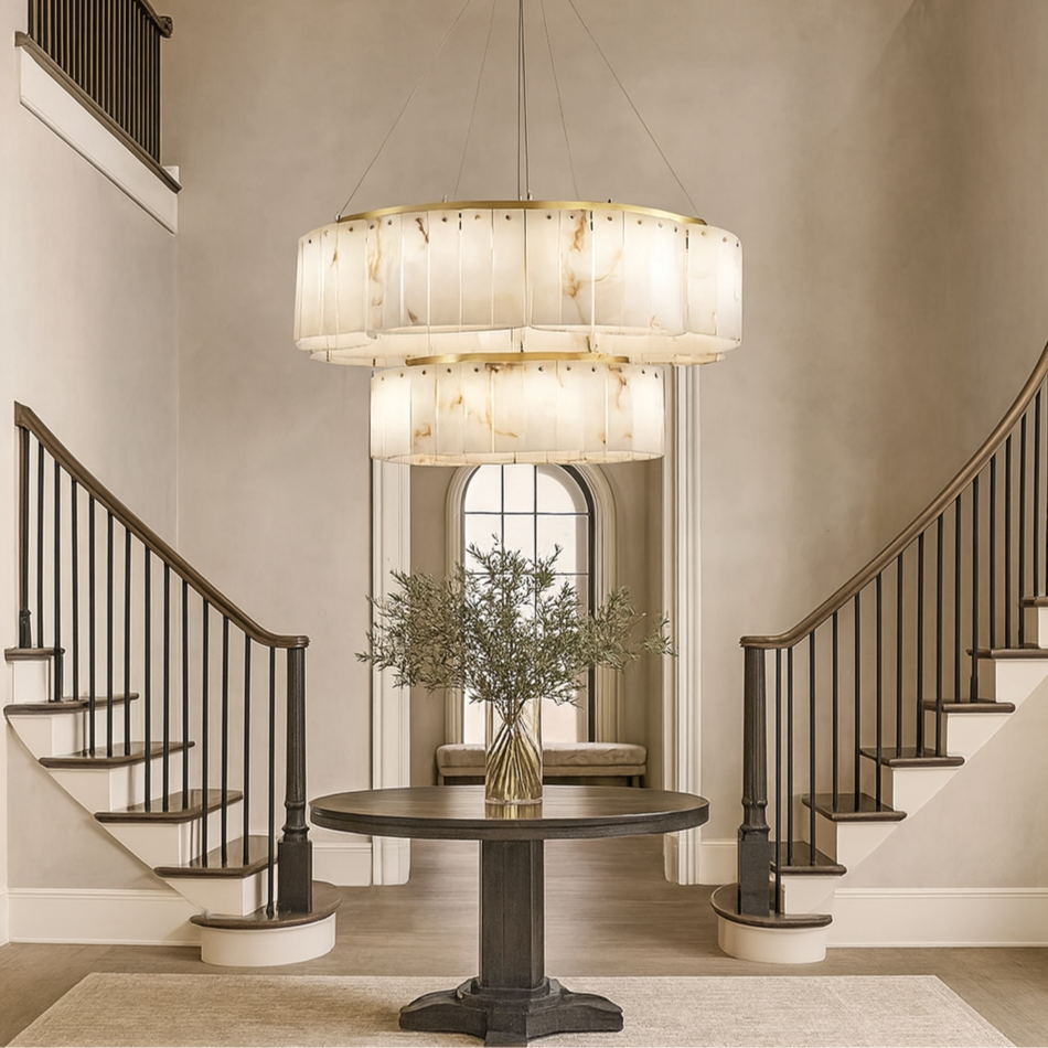 A grand entryway with twin curved staircases, a large round table with greenery, neutral-toned decor, arched doorway, and the Solenne Two-Tier Marble Chandelier by Morsale.com overhead.