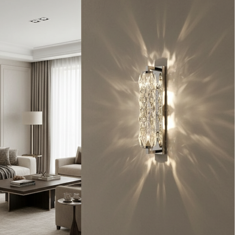 The Golford Crystal Sconce by Morsale.com features handmade crystals that cast intricate light patterns on a beige wall in a stylish living room with large windows, neutral sofas, a coffee table, and floor-length curtains.