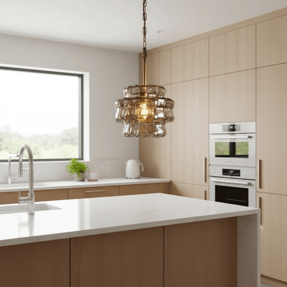 
                  
                    A modern kitchen with light wood cabinets, a white island countertop, built-in stainless steel appliances, a sink, and the Riviera Pendant by Morsale hanging above the island. Natural light enters through a window.
                  
                