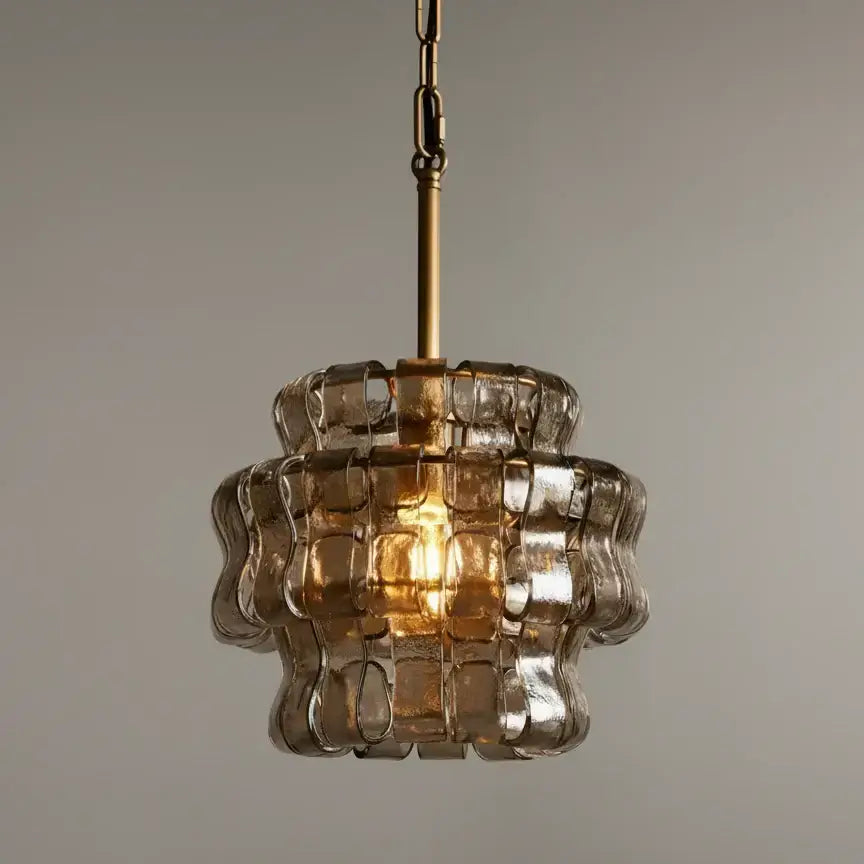 The Riviera Pendant by Morsale features a gold metal rod and an amber-tinted, wavy hand-blown glass shade, glowing warmly against a plain light gray background.