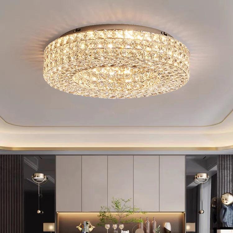 The Bacci Crystal Ceiling Light Fixture by Morsale, featuring LED bulbs, is elegantly installed on the ceiling, casting a warm glow. The illumination dances off the crystals, producing a sparkling effect. The room boasts modern decor with dark walls and offers a view of the dining area below.