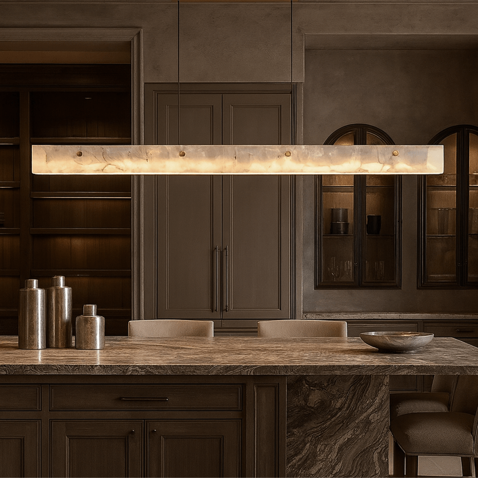 A modern kitchen features beige cabinetry, built-in shelves, and a Morsale Eterna Natural Marble Linear Chandelier above the marble island, which is adorned with decorative vases and a bowl.