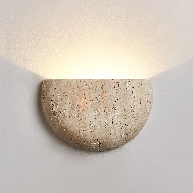 The Lina Natural Travertine Wall Light by Morsale.com features textured stone and an integrated LED, casting soft upward light against a light-colored wall.
