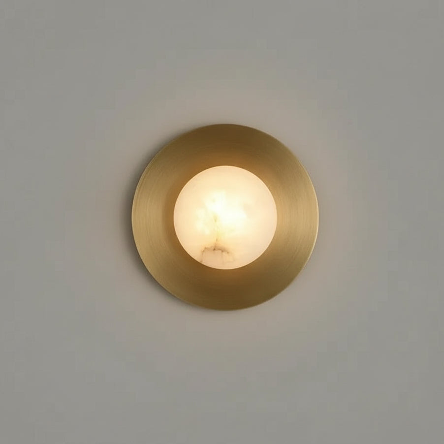 The Moonshade Brass & Marble Sconce by Morsale.com features a round LED bulb set in a brass circle with natural marble accents, offering a sophisticated glow and modern style against dark walls.