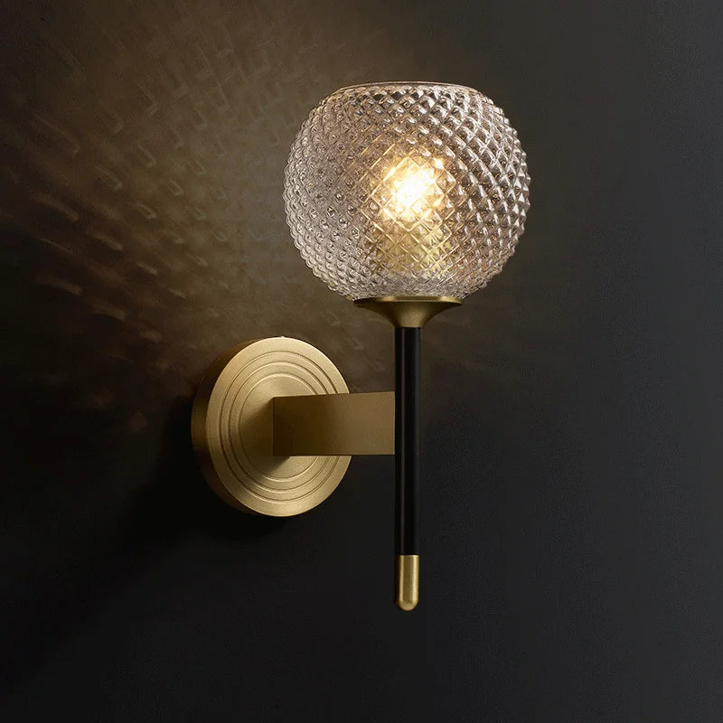 The image showcases the Palermo Wall Sconce Light by Morsale, featuring a modern design with a gold circular base and an arm extending outwards. At the end of the arm is a textured glass globe with a diamond-patterned cover that emits a warm light, creating an elegant appearance.