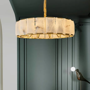 A modern, circular chandelier with white, marble-like panels and gold accents hangs from the ceiling. The background features dark green, paneled walls, adding a sophisticated and elegant touch to the space. This stunning Natural Marble Ceiling Chandelier by Morsale.com perfectly complements the room's refined aesthetics.