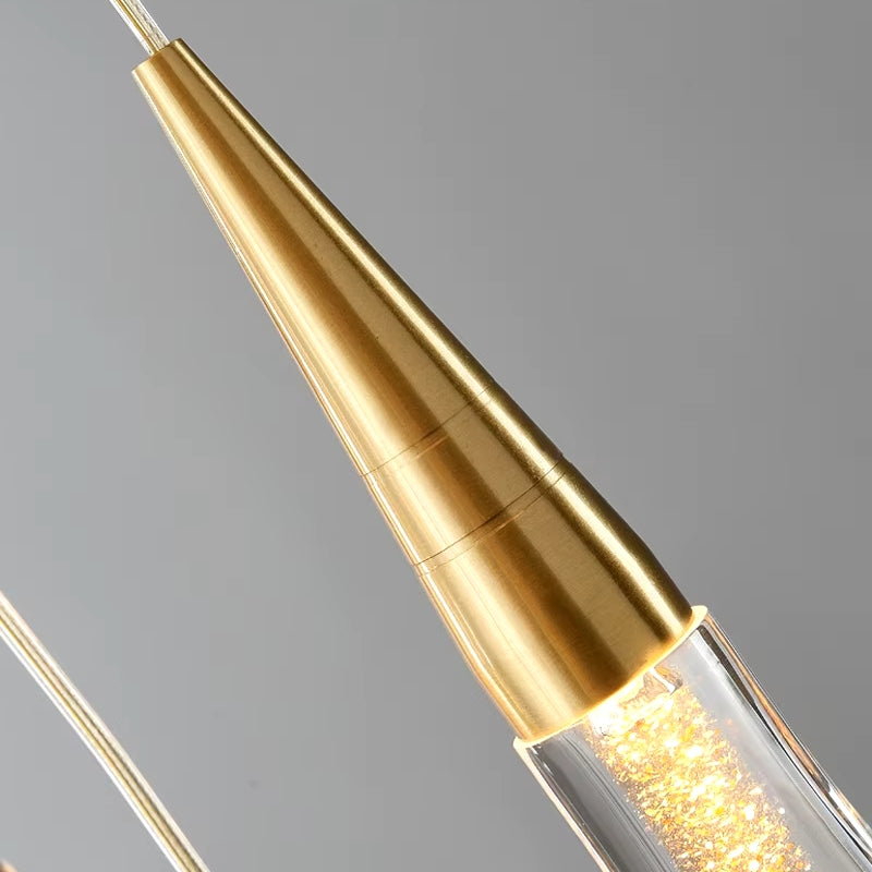 Close-up of the Pendant Light Fixture For Stairwell by Morsale.com, showcasing its modern design with a gold cone-shaped top adorned with gold specs. It features a transparent cylindrical body filled with sparkling elements, casting ambient light against a gray background.