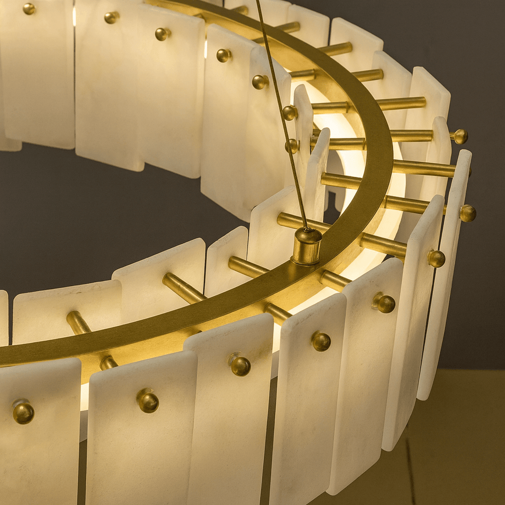 
                  
                    A close-up of the Lunaria Marble Chandelier by Bigman, a modern circular fixture with frosted rectangular glass panels on a gold frame, glowing warmly and evoking the look of refined Spanish marble lighting.
                  
                