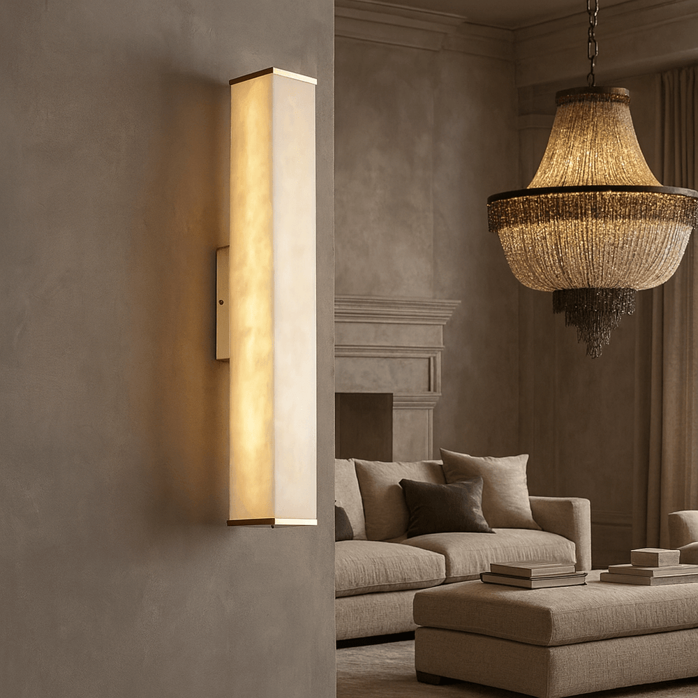 
                  
                    The Avana Marble Wall Sconce by Morsale.com casts a warm glow on a textured beige wall in a sophisticated living room with a beige sofa, neutral pillows, stacked books, and a large crystal chandelier.
                  
                