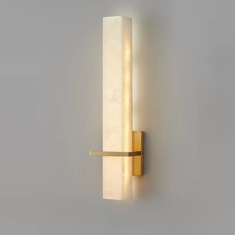 The Natural Marble Indoor Sconce from Morsale.com features a modern design with a slim, rectangular marble shade and a brass mounting base. It includes an LED light source that emits a warm glow and is positioned vertically on a neutral-colored wall.