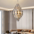 A modern living room showcases the Morsale Lazzo Crystal Chandelier with stainless steel accents, suspended above a curved beige sofa and round coffee table, all set against light vertical-paneled walls.
