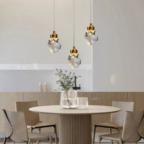 A contemporary dining room showcases a round wooden table accompanied by four beige chairs. Overhead, three Morsale Diamante Crystal Pendant Lights infuse the space with elegance. The table is adorned with a glass vase filled with greenery, while light-colored walls and minimal decor contribute to a tranquil atmosphere.