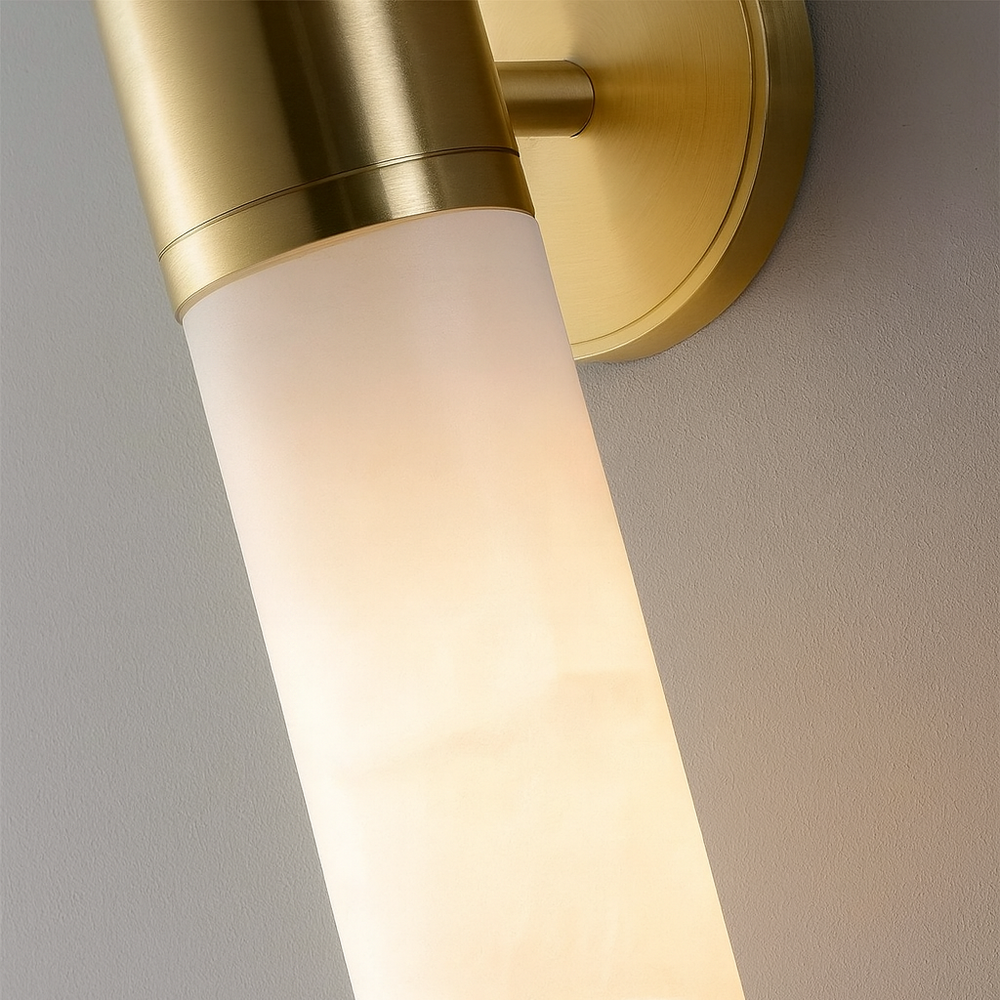 
                  
                    The Aurelia Natural Marble Wall Sconce by Morsale.com features a cylindrical frosted glass shade, solid brass hardware, and a brushed gold base. Mounted on a light wall, it emits soft, warm light—ideal for modern interiors.
                  
                