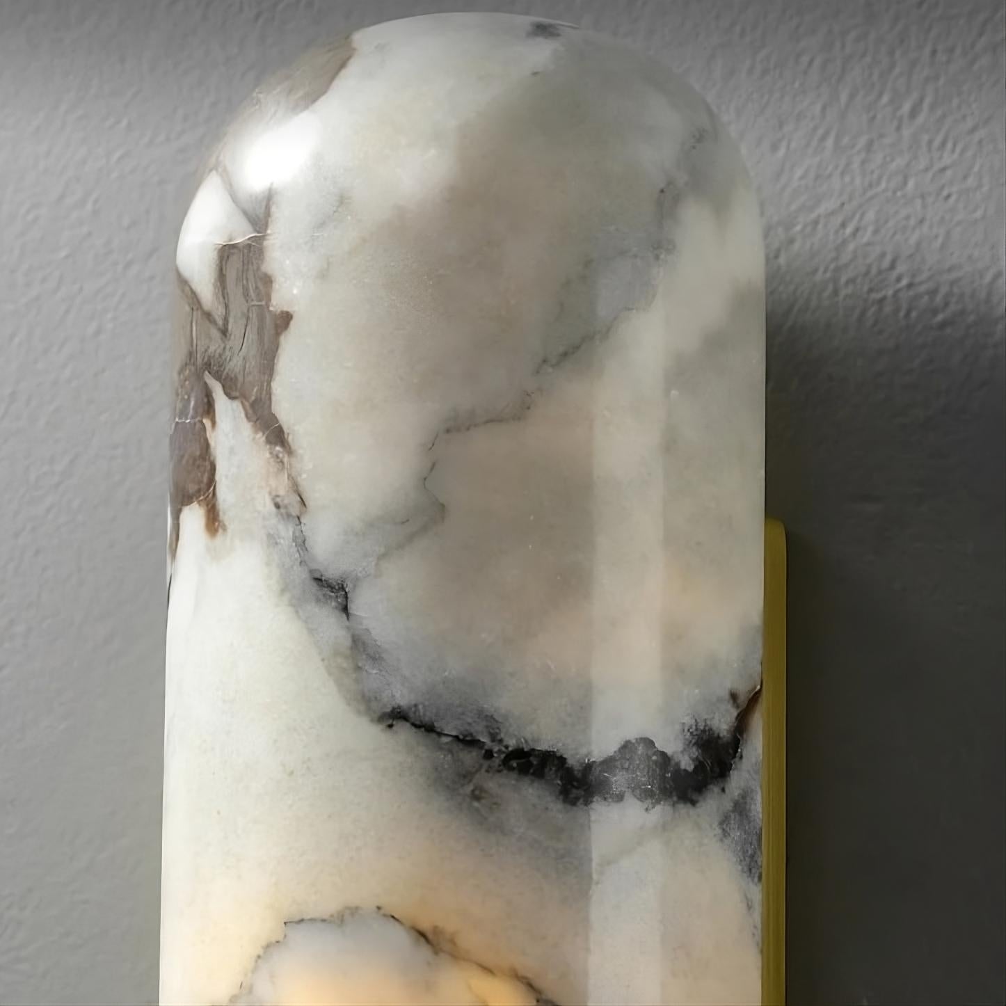 A close-up image of the Natural Marble Wall Sconce Light Fixture by Morsale.com made of natural marble. The unique patterned sconce features a polished, cylindrical surface with grey and white marble veining. The light subtly illuminates the stone from within, highlighting its texture and color variations.