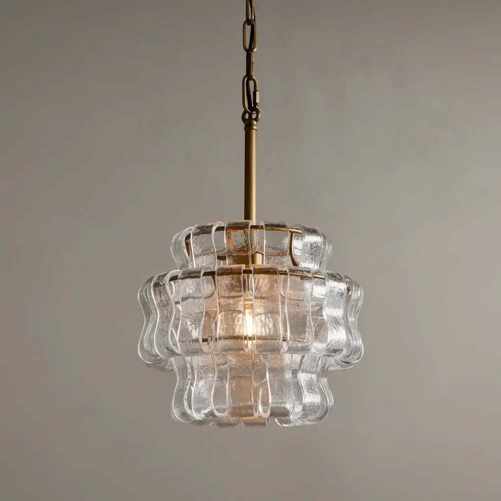 The Morsale Riviera Pendant showcases layered, wavy-edged glass panels and a gold chain, offering modern minimalist elegance against a plain beige backdrop.