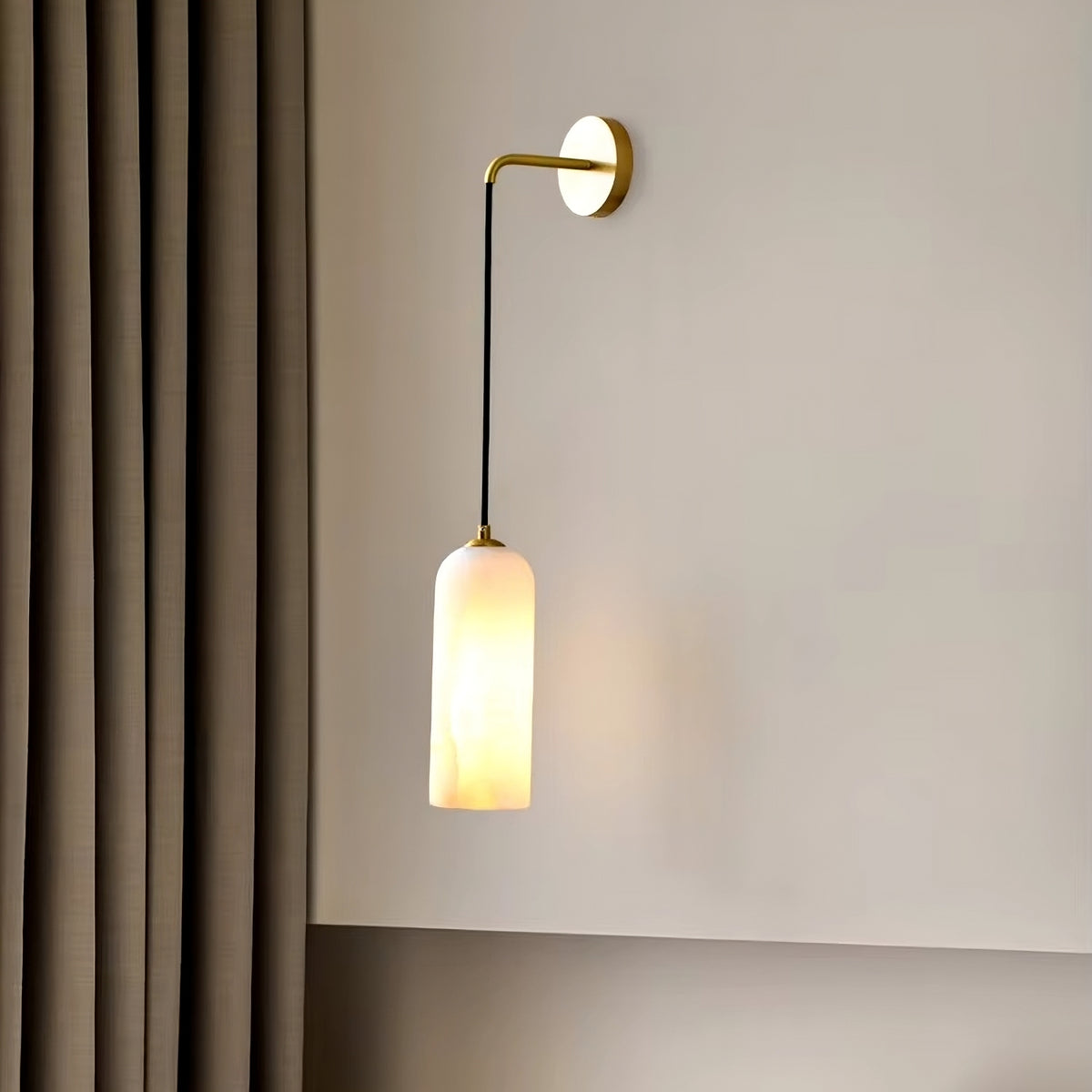 Mounted on a light gray wall, the Moonshade Natural Marble Wall Light by Morsale.com, featuring a gold arm and white cylindrical shade reminiscent of elegant wall sconces, casts a soft, warm glow. Nearby, a floor-length taupe curtain enhances the inviting ambiance of the home decor.