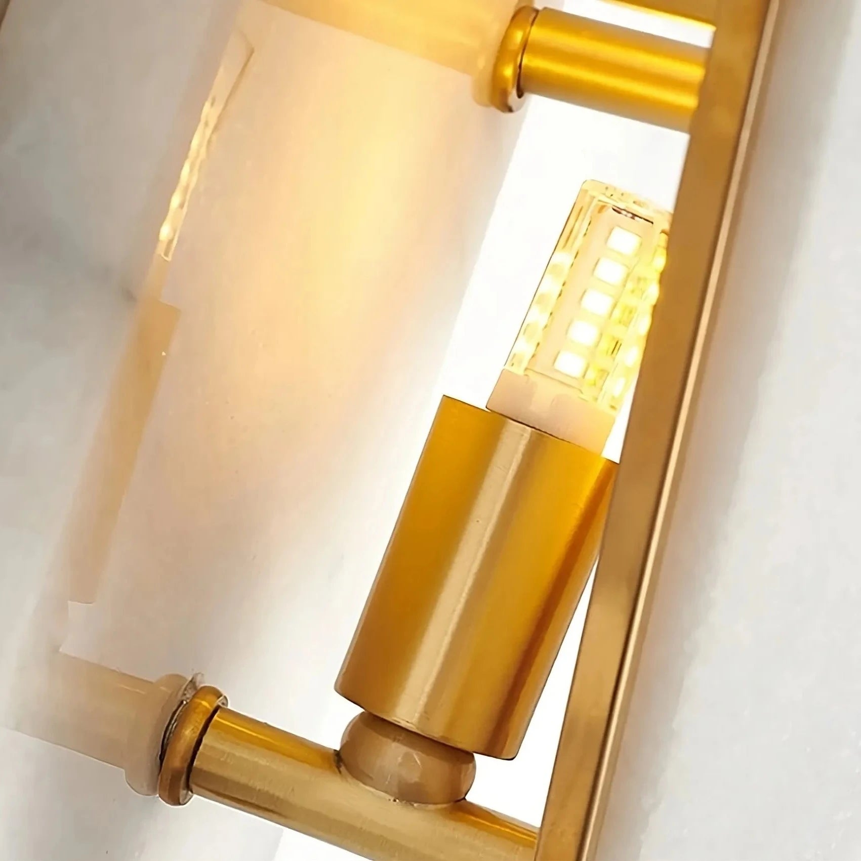 A close-up image of a modern lamp with a geometric design. The lamp features a gold metal frame and a light bulb encased in a perforated gold cylindrical holder, reminiscent of the elegance found in Bigman's Natural Marble Contemporary Wall Sconce Light, casting a warm glow against a light background.