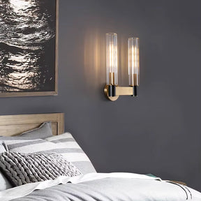 A contemporary bedroom showcases a wooden bed adorned with striped bedding and a textured gray pillow. Mounted on the dark gray wall is a sleek Morsale Palermo 2-Head Retro Brass Wall Sconce, providing warm lighting next to black and white abstract artwork.