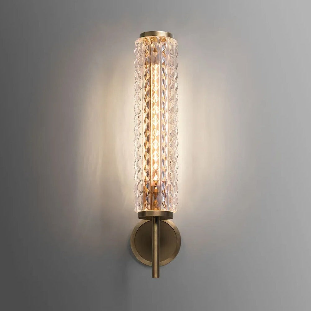 The Crystal & Copper Contemporary Wall Sconce by Morsale.com features a cylindrical, textured glass shade and a brass base, casting a warm glow against a grey wall background. This wall-mounted LED sconce seamlessly blends modern and vintage elements with contemporary aesthetics, adding an elegant touch to the surrounding decor.