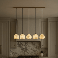 The Auris 5-Light Marble Chandelier by Morsale.com, featuring marble-patterned glass shades and adjustable cords, hangs above a kitchen island with beige cabinets and a marble backsplash in the background.