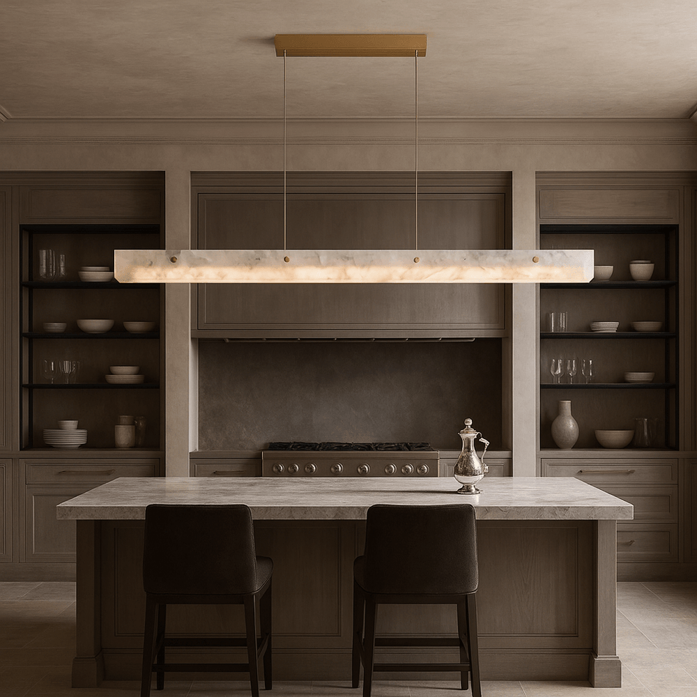 A minimalist kitchen features taupe cabinets, open shelves with white dishes, a marble island with two dark chairs, and the Morsale Eterna Natural Marble Linear Chandelier above. A silver teapot rests on the island.