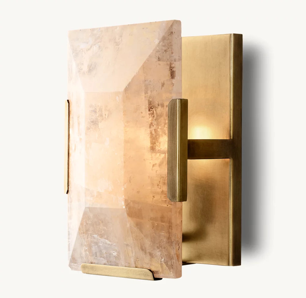 A stylish **Villano Calcite Crystal Wall Sconce** by **Morsale.com** featuring a rectangular, faceted glass panel set in a brass frame. The glass has a slightly rough texture, adding rustic charm. Light emanates softly from behind the glass, creating a warm, ambient glow. The overall design is minimalist and elegant, highlighting its handcrafted crystal precision.