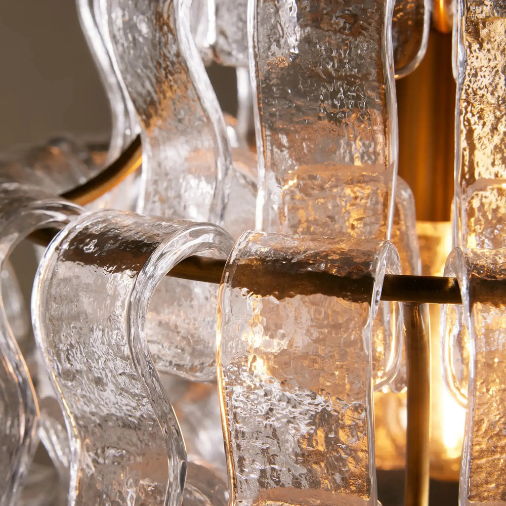 
                  
                    Close-up of the Morsale Riviera Pendant, a modern minimalist chandelier with textured clear glass ribbons gracefully curving around a warm bulb, supported by sleek metal rods.
                  
                