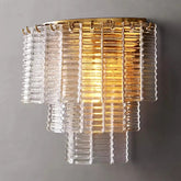 Presenting the Palermo Clear Crystal Wall Sconce from Chandelier Style, this chic fixture features tiered, ribbed glass panels in clear and amber hues. Luxurious crystal accents create a warm glow that elevates the modern and elegant design against a plain gray wall.