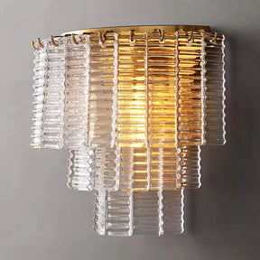 Presenting the Palermo Clear Crystal Wall Sconce from Chandelier Style, this chic fixture features tiered, ribbed glass panels in clear and amber hues. Luxurious crystal accents create a warm glow that elevates the modern and elegant design against a plain gray wall.