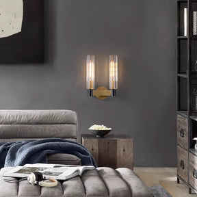 A modern living room showcases a cushioned lounge chair draped with a blue blanket, accompanied by a wooden side table holding a bowl. Luxury lighting from the Morsale Palermo 2-Head Retro Brass Wall Sconce beautifully illuminates the dark gray wall. Above the chair hangs an abstract art piece, adding to the contemporary ambiance.