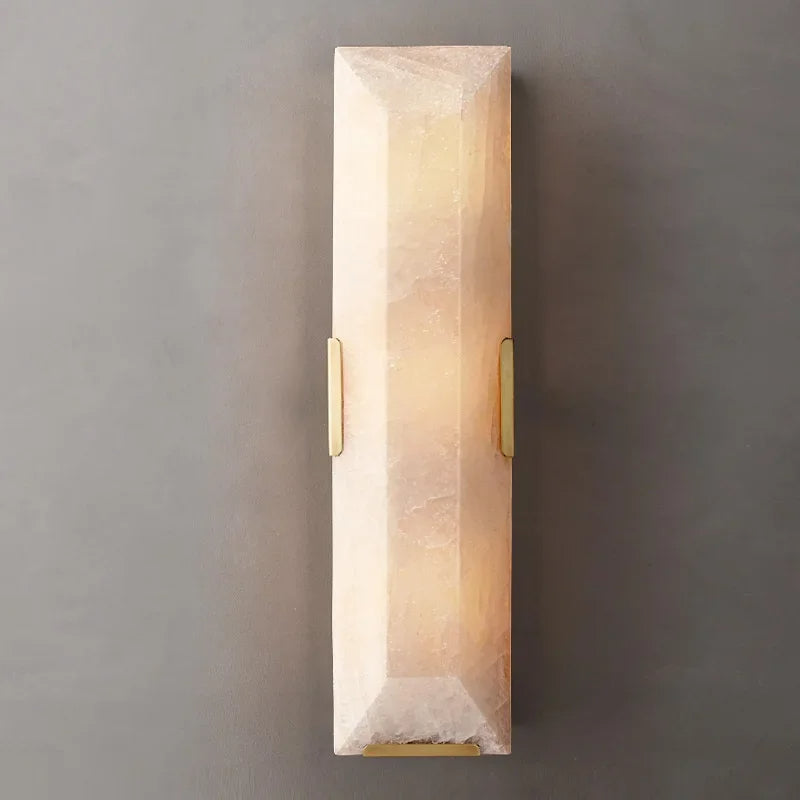 
                  
                    The Brookhill Calcite Wall Sconce by Morsale.com is a rectangular, faceted wall light made of translucent pale pink material, glowing with warm light and mounted on a gray wall with two small brass brackets.
                  
                