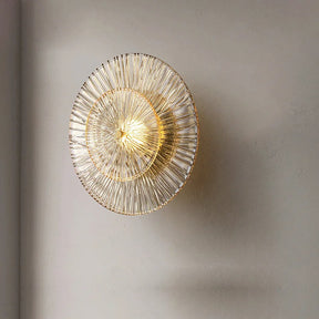 A Modern Glass Wall Sconce from Morsale.com is mounted on a plain, light-colored wall. The light emits a warm glow through the intricate, radial wire design, casting soft shadows on the wall—a true testament to artisanal craftsmanship.