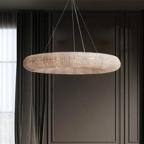 In a contemporary living room, a Bergamo Crystal Modern Chandelier from Morsale.com hangs gracefully from the ceiling. Its exquisite crystals brighten the dark walls, while a grey couch adorned with cushions is positioned beside a small table and floor-length curtains, creating an elegant and welcoming ambiance.