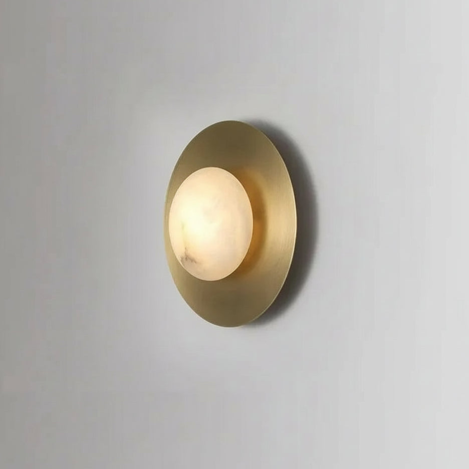 The Moonshade Brass & Marble Sconce from Morsale.com features a circular brass base and spherical frosted glass shade, casting a soft, warm glow on any light gray wall—ideal for accenting contemporary interiors.