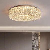 The Morsale Bacci Crystal Flush Mount Ceiling Light is installed on a modern white ceiling, casting an elegant warm LED glow in a contemporary room with neutral walls and a marble accent.