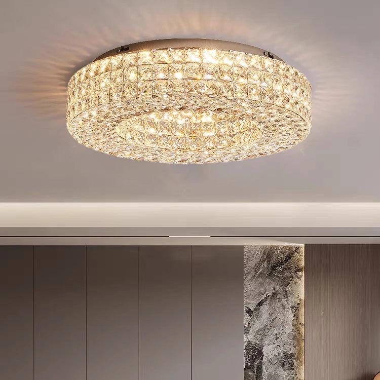 The Morsale Bacci Crystal Ceiling Light Fixture graces the room with its round, modern luxury design, casting a sparkling glow that bathes the neutral-toned ceiling and textured accent walls in warmth.