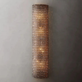 The Bergamo Crystal Wall Sconce by Morsale.com features a cylindrical design adorned with numerous small, clear crystals. Several dimmable LED bulbs illuminate it from within, supported by a sleek stainless steel frame, casting a warm and elegant glow against a neutral wall.