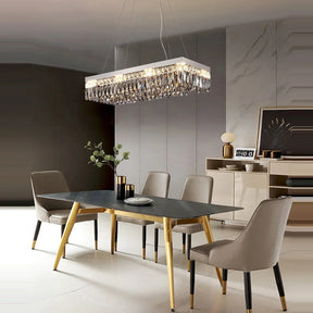 A modern dining room features a rectangular black table with gold legs, surrounded by four taupe upholstered chairs. A stylish Giano Crystal Ceiling Light by Morsale.com hangs overhead. A minimalist sideboard, decor items, and a large framed artwork adorn the background.