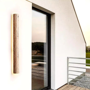 Next to a large glass door on the modern building exterior, the minimalist YEBMLP IP65 Waterproof Natural Travertine Wall Light adds an energy-efficient touch. This white fixture with a wooden accent is beautifully set amidst lush greenery, creating a scenic backdrop.